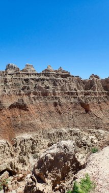 Uzun katmanlı uçurumlar ve sivri kaya oluşumları aşınma ve güneş ışığıyla yontulmuş kuru bir kanyonun üzerinde yükselir.