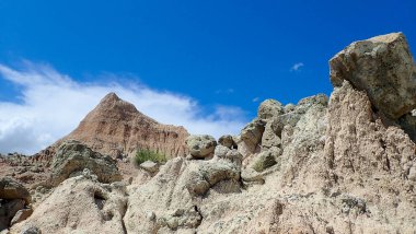 Keskin çorak topraklar kayalar ve kayalar parlak mavi gökyüzü ve bulutların altında uzak bir tepeye doğru yol alır.
