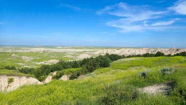 Geniş çimenli çayır, yazın açık mavi gökyüzünün altında aşınmış çorak arazi kayalıklarıyla buluşur.