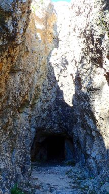 Sarp kayalıklara oyulmuş, gölgeler ve doğal kaya dokularıyla çevrili dramatik bir taş tünel.
