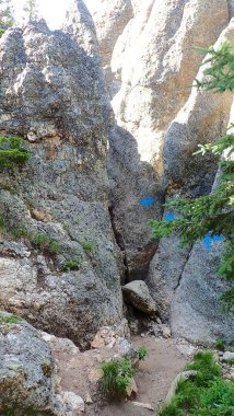 Dar kaya yarığı, engebeli taş ve çam dallarıyla çerçevelenmiş mavi iz boyasıyla işaretlenmiş.