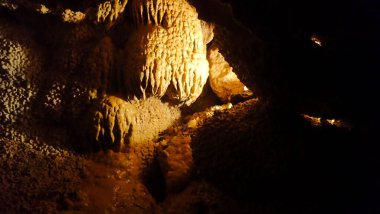 Flowstone formation resembling melted wax, illuminated within the depths of Jewel Cave to highlight its glossy texture and natural shapes.