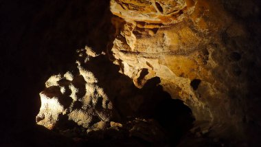 Mücevher Mağarası 'nın içinde zıt dokulara ve katmanlı oluşumlara sahip loş ışıklı kaya geçitleri spot ışıklarıyla aydınlatılıyor..