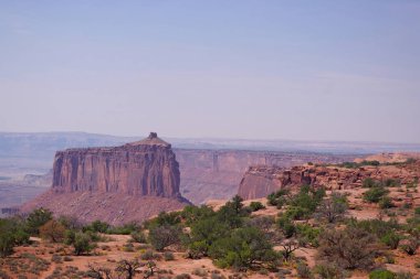 Kızıl kaya tepesi, Kanyonlar Ulusal Parkı, Utah 'ta çölün üzerinde dramatik uçurumlar, kanyon duvarları ve berrak bir gökyüzünün altındaki kurak bitki örtüsüyle yükselir..