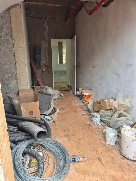 Kapalı bir inşaat alanının görüntüsü, enkaz, PVC borular, alet kutusu ve boya kutularıyla düzensiz bir koridor gösteriyor, binadaki bir projenin hissini ve dönüşüm aşamasını yakalıyor..