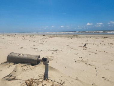 An old car exhaust abandoned on the beach A clean beach with an exhaust thrown in the corner, highlighting the importance of keeping beaches clean and recycling. clipart