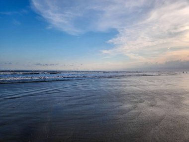 Akşamın ilerleyen saatlerinde sahilde alacakaranlıkla, arkasında güzel mavi bir okyanus ve bulutlu bir gökyüzü.