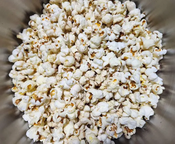 Cömert bir porsiyon gevrek, altın patlamış mısır, mükemmel bir şekilde patlamış ve gümüş bir kasede ayarlanmış. Beyaz ve altın patlamış mısır arasındaki zıtlık karşı konulmaz bir cazibe yaratıyor..