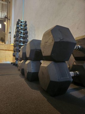 Modern bir spor salonunda sıralanmış siyah kauçuk halterlerin detaylı görüntüsü antrenman ve spor için ayrılmış bir alanı yansıtıyor..