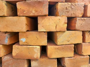 Katmanlar halinde düzenlenmiş turuncu seramik tuğlalar. Tuğlalar farklı dokulara ve ışığı ilginç bir şekilde yansıtan düzensiz yüzeylere sahiptir..