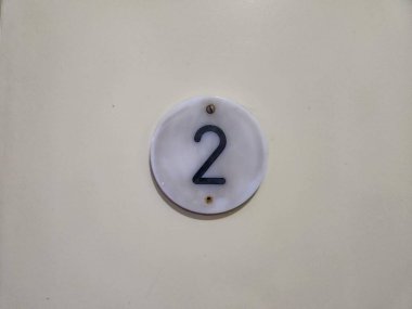 Işık duvarı yüzeyine asılmış iki numaralı bir plaket. Plaket daireseldir ve arkaplan ile zıt dokuların bir kombinasyonunu içerir..