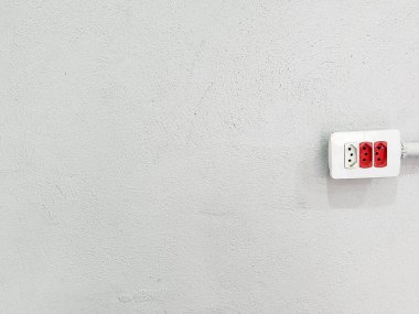 Desenli gri bir duvara monte edilmiş üç prizli modern bir elektrik prizi. Prizde, çağdaş ve işlevsel bir tasarımı sembolize eden iki kırmızı soket yer alıyor..