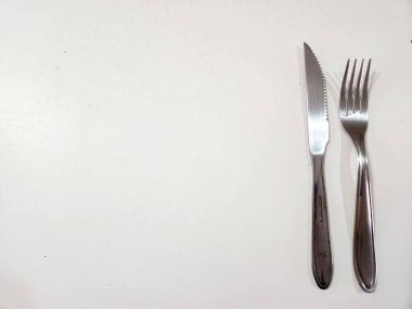 Beyaz bir yüzeyde dikey sıralanmış paslanmaz çelik çatal ve bıçağı gösteren minimalist bir resim..