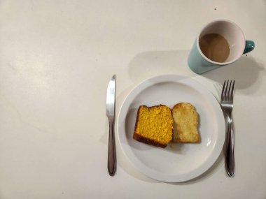 Bir dilim sarı pastayla basit ve rahat bir kahvaltı, bir fincan buharlı kahveyle eşleştirilir..