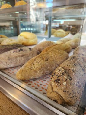 Bir fırın vitrininde sergilenen çeşitli taze ekmekler zengin bir dokuyu ve altın kabuğu vurguluyor..