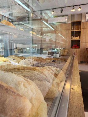 Modern bir fırın, sıcak ve davetkar bir atmosfer yaratmak için sıcacık aydınlatılmış baget ve rustik somunlar gibi çeşitli taze ekmekleri sergiliyor..