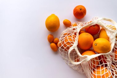 Beyaz arka planda bir sicim torbasında parlak narenciye meyveleri ve yakınlarda birkaç meyve var. Kavram: Tüm aile için sağlıklı beslenme ve kış meyveleri.