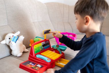 Pofuduk bir koyunun elinde oyuncak bir kredi kartı tutarken, çocuk hevesle parlak bir oyuncak kasasıyla dükkancılık oynuyor. Hayal gücü geliştirme ve rol yapma oyunları kavramı.
