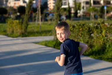 Kolunda glukoz sensörü olan bir çocuk scooterla kameraya gülümsüyor. Konseptler: çocukluk sevinci ve enerji, diyabet, tıbbi teknoloji, aktif yaşam tarzı.