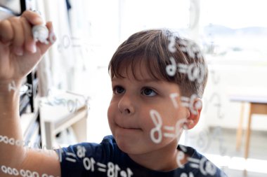 Yetenekli bir çocuk cam üzerine keçeli kalemle matematiksel formüller yazar. Konseptler: yetenekli çocuklar, BTMM eğitimi, alternatif öğrenme yöntemleri, bilim ve teknolojinin geleceği.