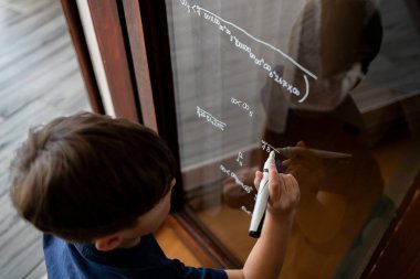 Çocuk bardağa bir kalemle matematiksel formüller yazıyor. Konseptler: nöroçeşitlilik, özel ilgi, matematiksel araştırma, matematik tutkusu, geleneksel olmayan öğrenme.