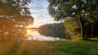 Sakin bir gölün üzerinde gün batımı parlak turuncu ve altın renkleri yansıtıyor.