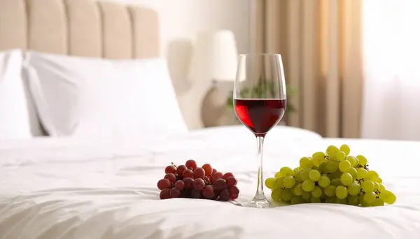 kırmızı şarap bardakta ve yatakta meyveler