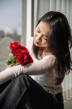 Camdan kırmızı güller kokan Asyalı bir kız. Yüksek kalite fotoğraf