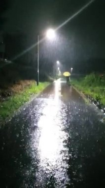 Bir adam gece bir sokak lambasının altında şemsiyeyle yağmurda yürür. Yüksek kalite 4k görüntü