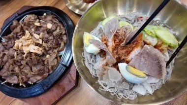 Kore usulü soğuk erişte, naengmyeon. Dilimlenmiş salatalık, turp turşusu. Lezzetli yemekler. Yüksek kalite 4k görüntü