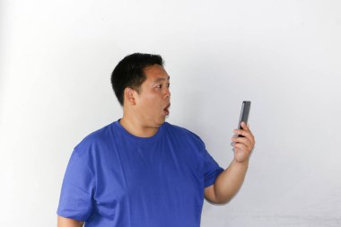 Mavi tişört giyen şaşırmış adam izole edilmiş beyaz arka planda telefona bakıyor.