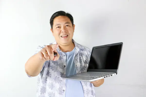 Mutlu Asyalı adam dizüstü bilgisayar tutuyor ve beyaz arkaplandaki kopyalama alanını işaret ediyor.