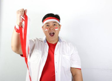 Kırmızı tişört ve kırmızı kravat giyen Asyalı genç adam kırmızı beyaz kurdele tutuyor ve mutlu bağımsızlık gününü kutluyor.