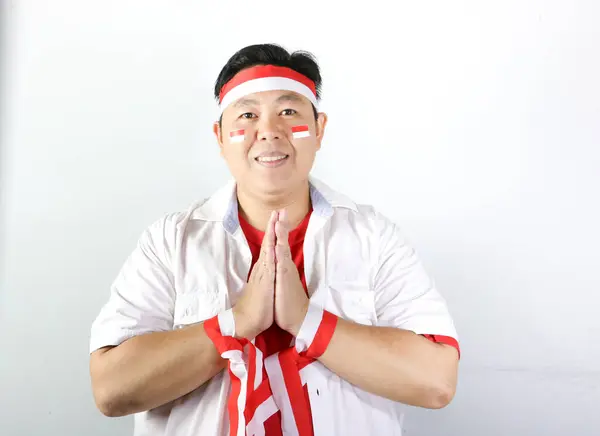 Yüzünde gülümseme olan beyaz gömlekli ve kırmızı pantolonlu Asyalı adam namaste pozu veriyor.