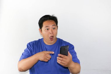 Beyaz arka planda duran akıllı telefonlu, şok olmuş Asyalı adam..