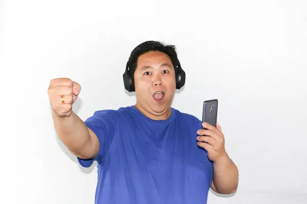 Asyalı adam akıllı telefon tutuyor ve beyaz arka planda zafer jesti yapıyor.