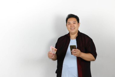 Elinde para ve telefon tutan gülümseyen Asyalı adam.