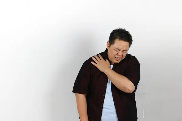 Omuz ağrısı çeken genç Asyalı adam beyaz arka planda izole edilmiş..