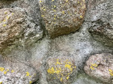 Sarı yosun bantları ve pürüzlü dokusu olan yıpranmış taş duvarın yakın çekimi