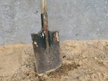 Tahta saplı metal kürek sert beton duvarın yanında duruyor.