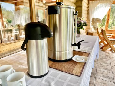 Paslanmaz çelik kahve ve çay makinesi parlak bir yemek odasında fincanlarla dolu bir masada.