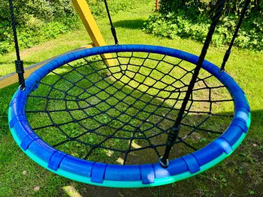 Güneşli bahçede sallanan mavi yuvarlak ağ salıncağı