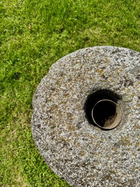 Eski yuvarlak taş değirmen çarkı, ortasında bir delik çimlerin üzerinde yatıyor.