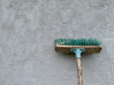 Ahşap saplı klasik süpürge ve gri beton duvara yaslanmış yeşil kıllar.