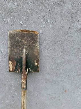 Gri desenli beton arka plana yaslanmış ahşap saplı paslı kürek.