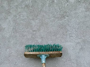 Ahşap saplı klasik süpürge ve gri beton duvara yaslanmış yeşil kıllar.