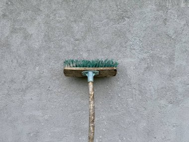 Ahşap saplı klasik süpürge ve gri beton duvara yaslanmış yeşil kıllar.