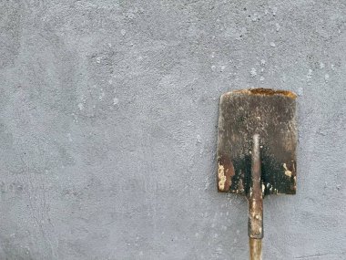 Gri desenli beton arka plana yaslanmış ahşap saplı paslı kürek.