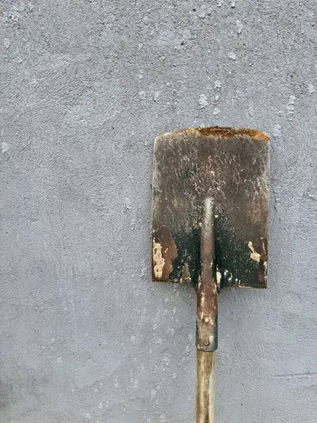 Gri desenli beton arka plana yaslanmış ahşap saplı paslı kürek.