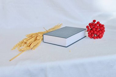 Siyah kitap, buğday kulakları ve beyaz arka planda kırmızı yapay çiçek.